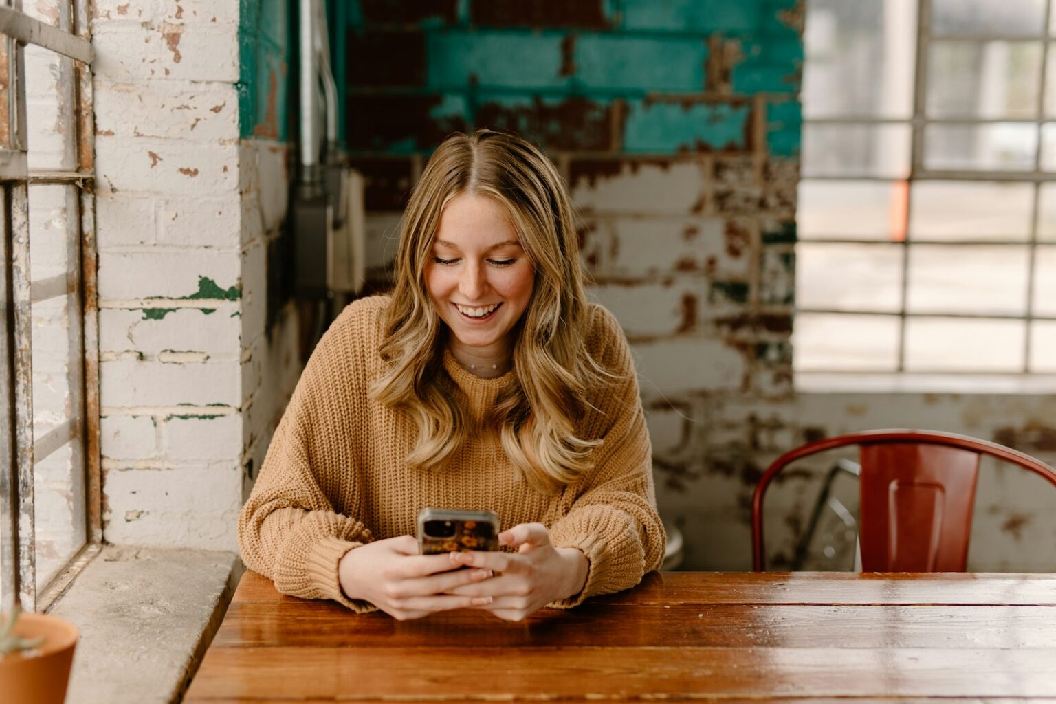 Smiling woman sitting at a table reading a text message on her phone