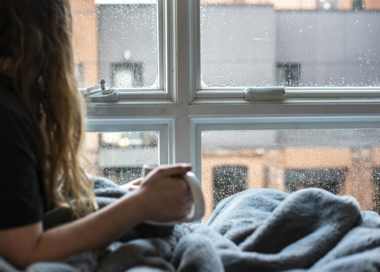 Woman in a gray sweater sitting by the window at home