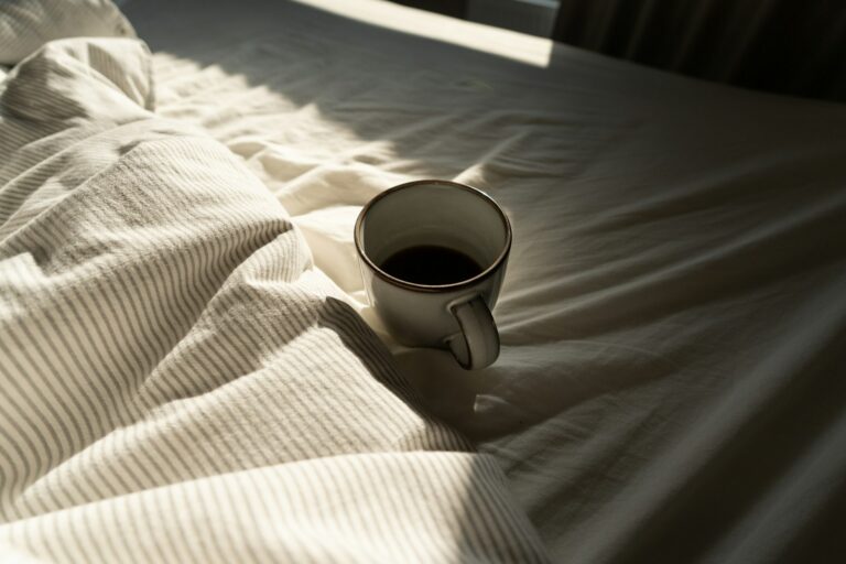 Cup of coffee on white bed sheets in the morning light