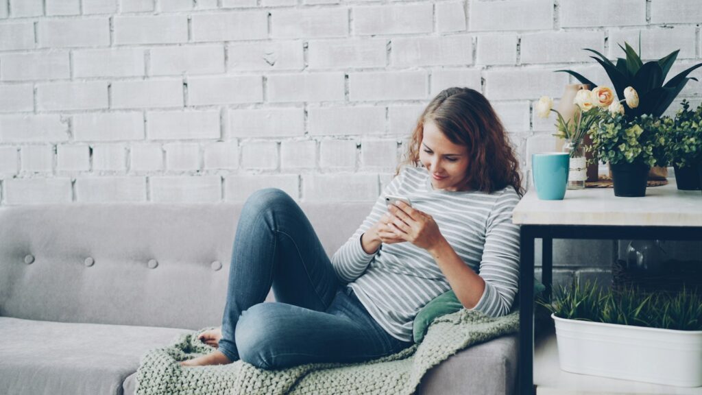 Young woman smiling at her smartphone on the couch