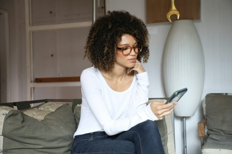 Thoughtful woman sitting at home looking at her phone