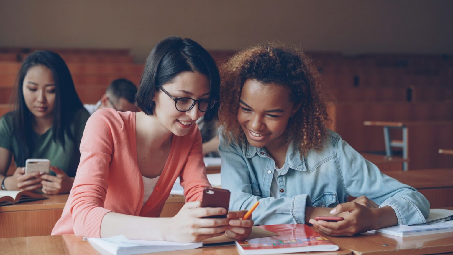 Two students smiling while looking at a smartphone